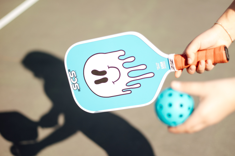 A person holding a paddle with a blue and white design, showcasing the best grips for an elevated pickleball game. Improve your hold and control on the court today.