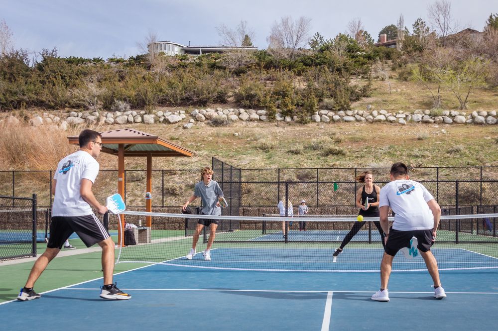Four people playing pickleball on a court with a hill in the background.