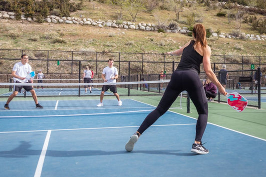 A woman in black leggings plays pickleball with a men, showcasing the difference between indoor vs outdoor pickleball.