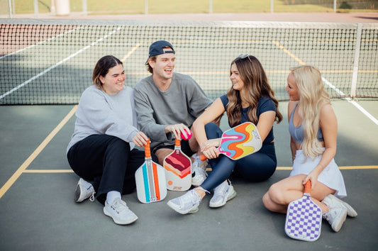 Four youths with pickleball rackets seated on the court, ready to play.