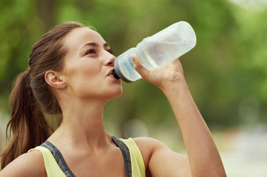 A woman drinking water from a bottle, emphasizing hydration for pickleball.
