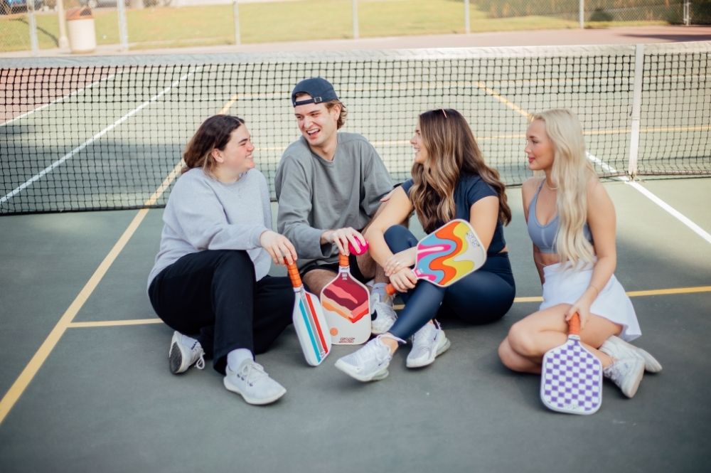 A group of four young individuals laughing together showing the benefits of pickleball mental health.