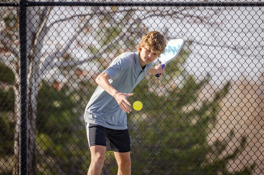 A young man hits a pickleball while participating in a youth pickleball program.