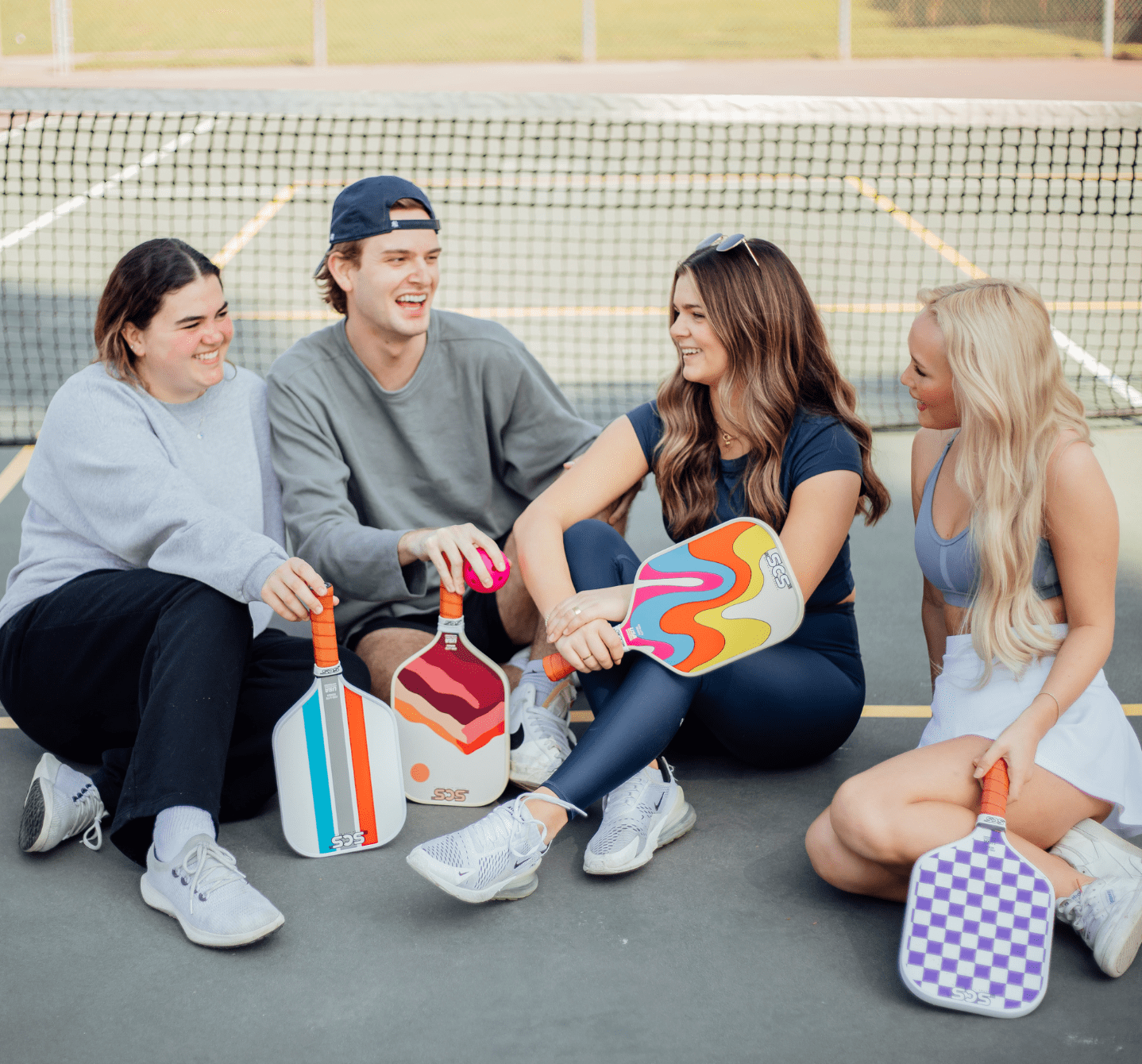 SCS Pickleball team members laughing on a pickleball court holding custom pickleball paddles