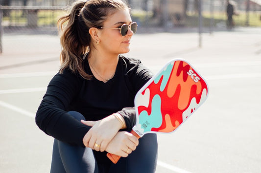 A young lady sits on a pickleball court holding a custom pickleball paddle
