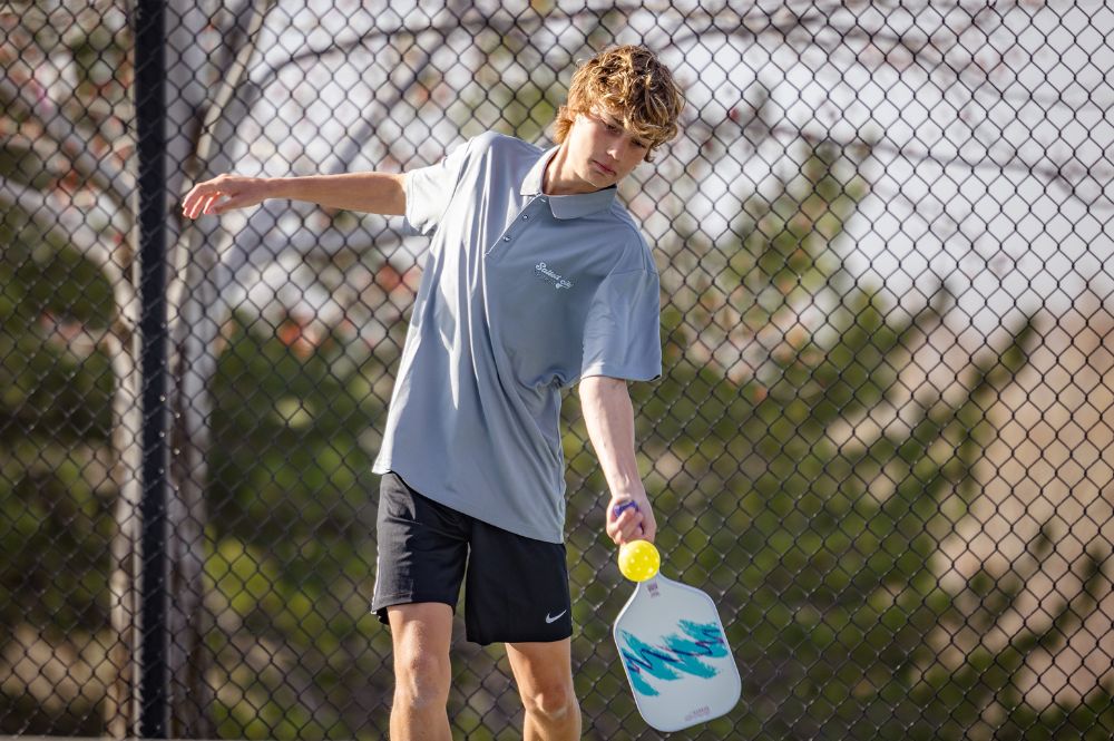 Pickleball player focusing on the ball mid-swing, demonstrating improved hand-eye coordination on a sunny outdoor court