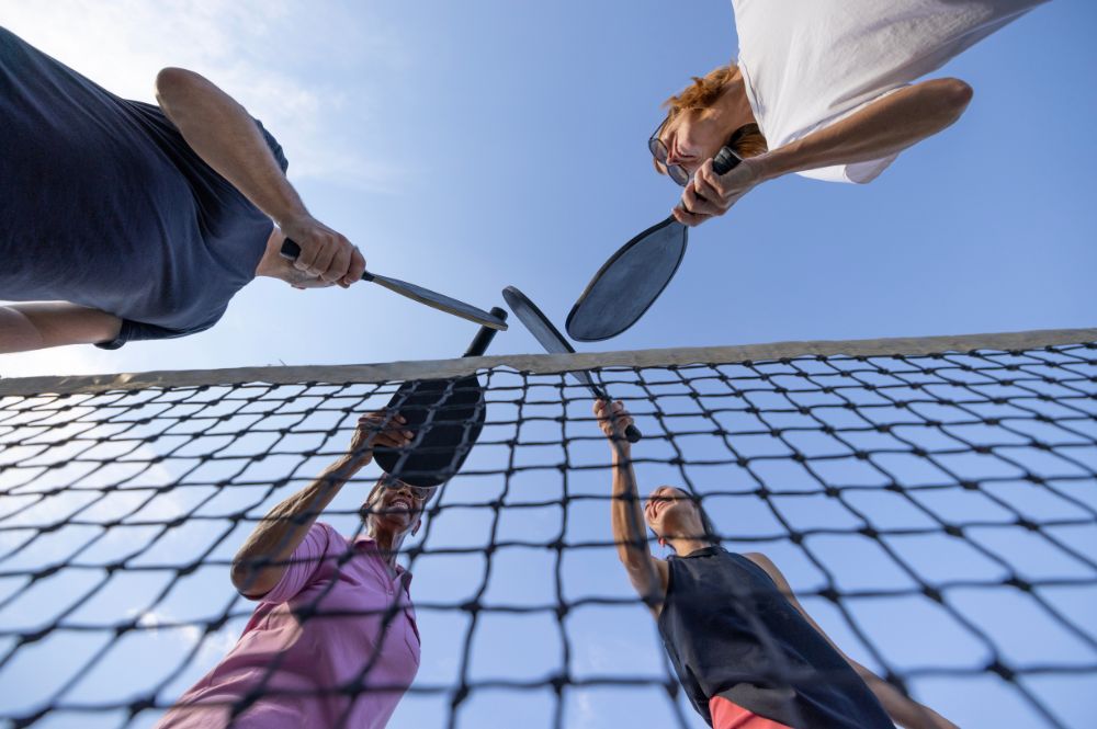 Three individuals engaged in a game of international pickleball at a net, showcasing athleticism and teamwork.