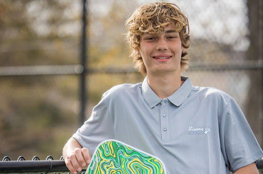 A young man holding a pickleball paddle.