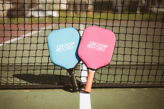 Two pickleball paddles leaning against a net, representing important equipment one would find in a pickleball gear guide.