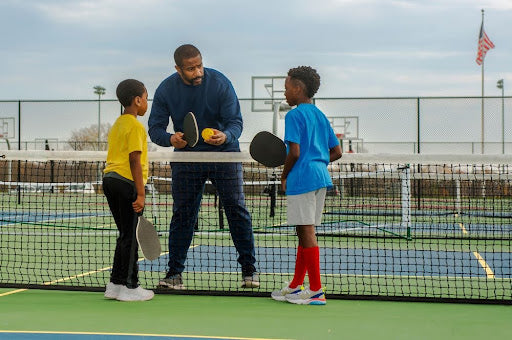 Pickleball coach showing two young boys how to play the game.