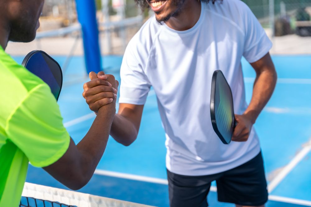 Two men shaking hands on a Pickleball court showing sportmanship in pickleball.