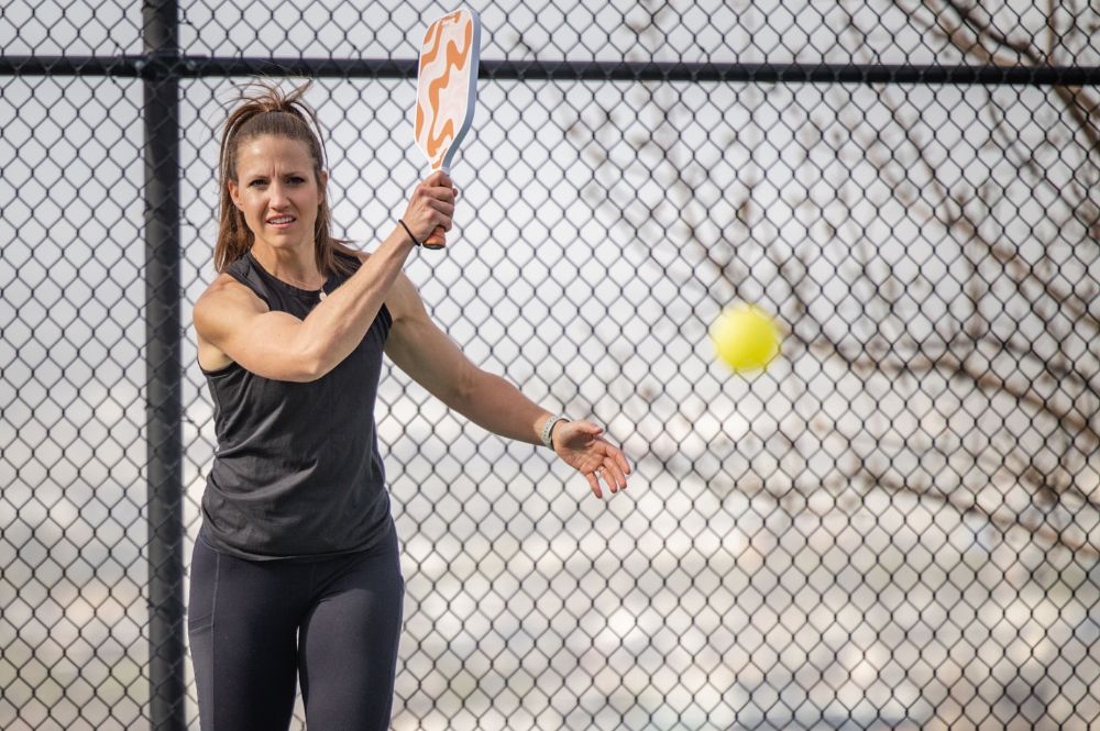 A woman playing pickleball, swinging a racket to hit a ball on a court.