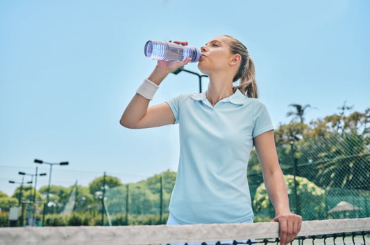 Female athlete drinking water during pickleball match.