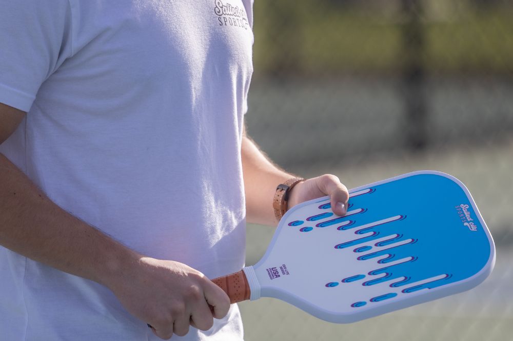 A man with a blue and white paddle highlights the best custom pickleball paddles for enthusiasts.
