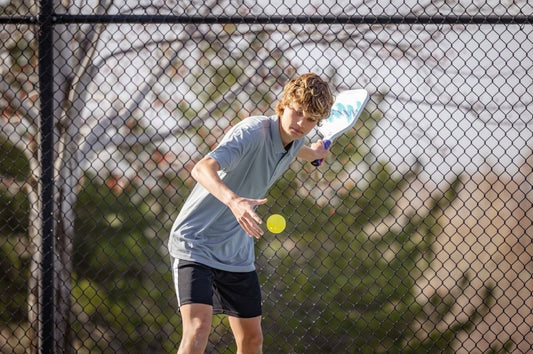 A young practicing pickleball serving techniques during a match.