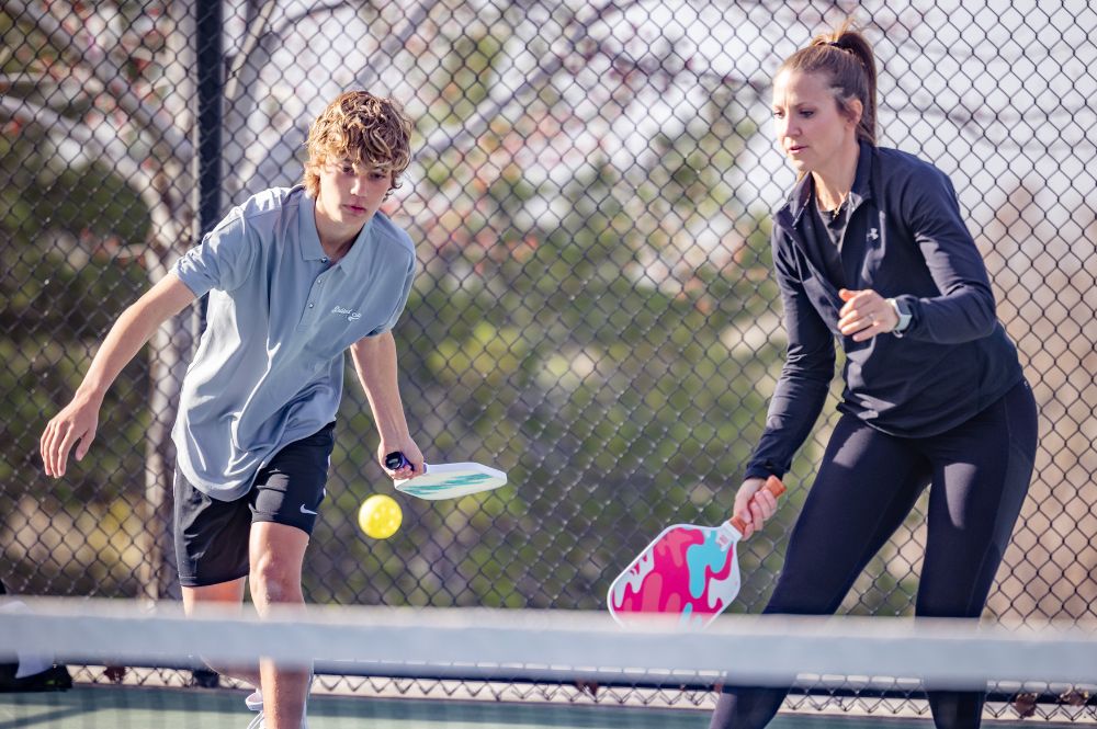 A woman and a boy engage in a lively game of tennis on a court, showcasing pickleball singles vs doubles dynamics.