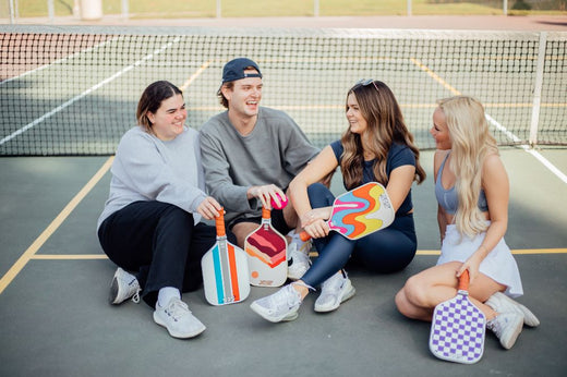 Four young people seated on the ground with tennis rackets, enjoying the social benefits of pickleball together.