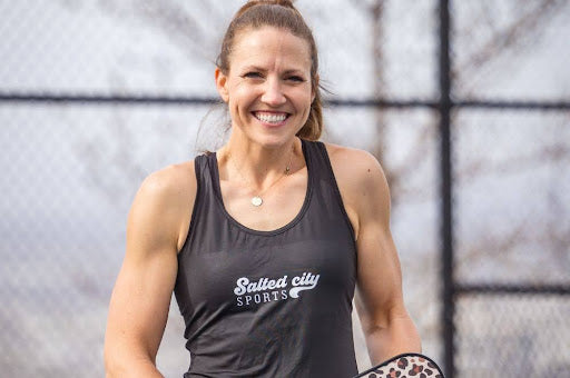 A young woman holding a pickleball paddle and smiling. 