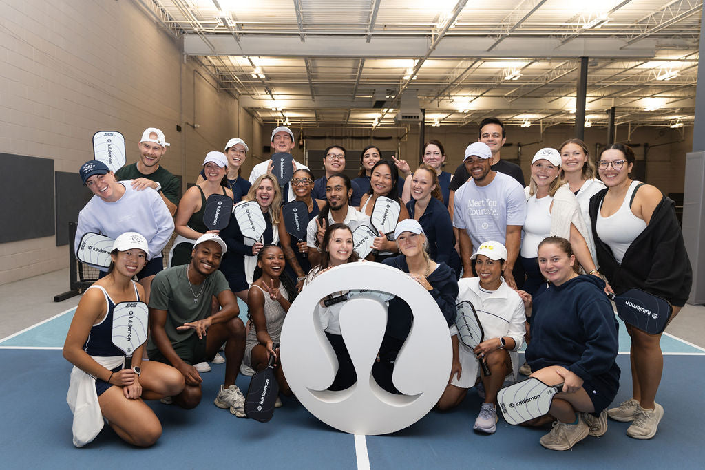 Corporate event with employees posing on a court holding custom branded pickleball paddles